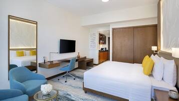 A hotel room with a large bed, a desk, a chair, a TV, and a small table.