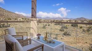 A balcony with wicker furniture, a glass table with a decorative tray, and a desert view. - Dusitd2 Naseem Resort Jabal Akhdar (Sayq)