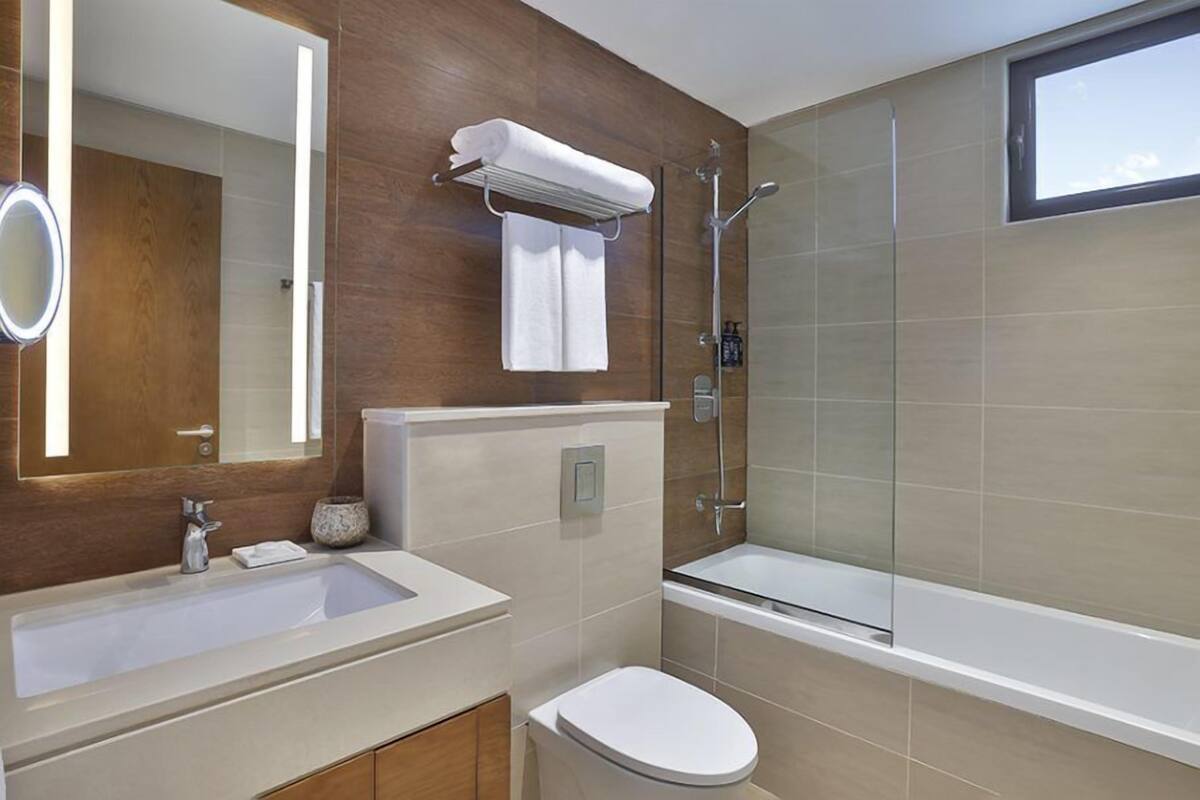 A modern bathroom with a large mirror, a sink, a toilet, and a glass-enclosed shower.