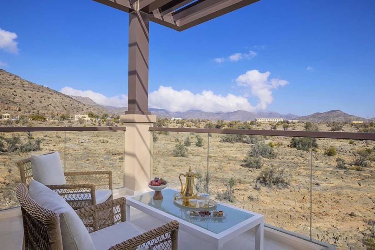 A balcony with wicker furniture, a glass table with a decorative tray, and a desert view.