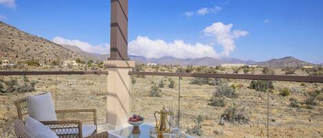 Un balcón con mobiliario de mimbre, una mesa de vidrio con una bandeja decorativa y vistas al desierto.