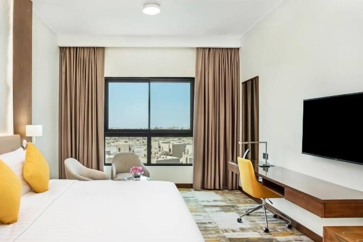 A hotel room with a bed, a desk, a chair, a TV, and a window with curtains.