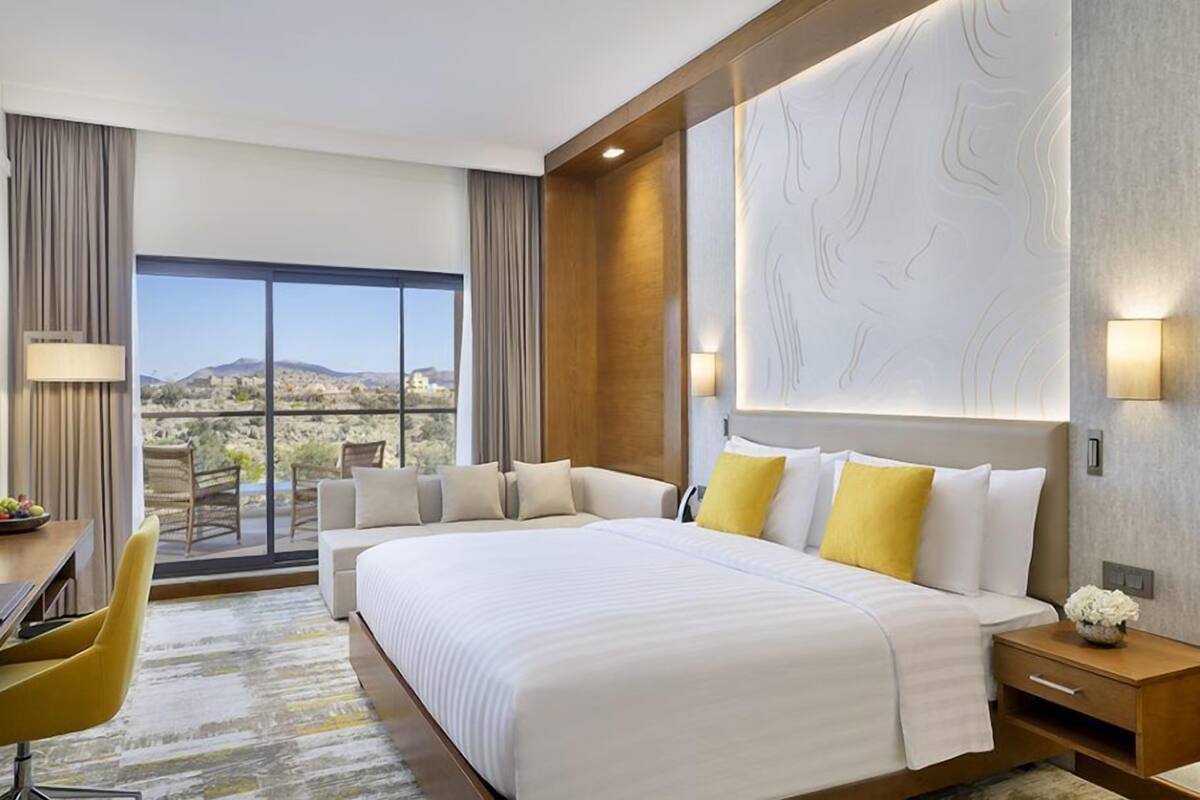 A hotel room with a large bed, a desk, a chair, and a view of the desert.