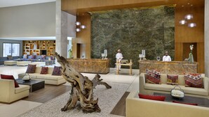A spacious lobby with a reception desk, sofas, a large decorative wall, and a wooden tree trunk centerpiece. - Dusitd2 Naseem Resort Jabal Akhdar (Sayq)