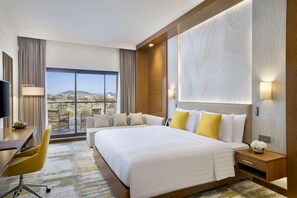 A hotel room with a large bed, a desk, a chair, and a view of the desert landscape. - Dusitd2 Naseem Resort Jabal Akhdar (Sayq)