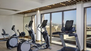 Un gimnasio con cintas de correr, elípticas y bicicletas estáticas, ventanas amplias y vistas de la ciudad.