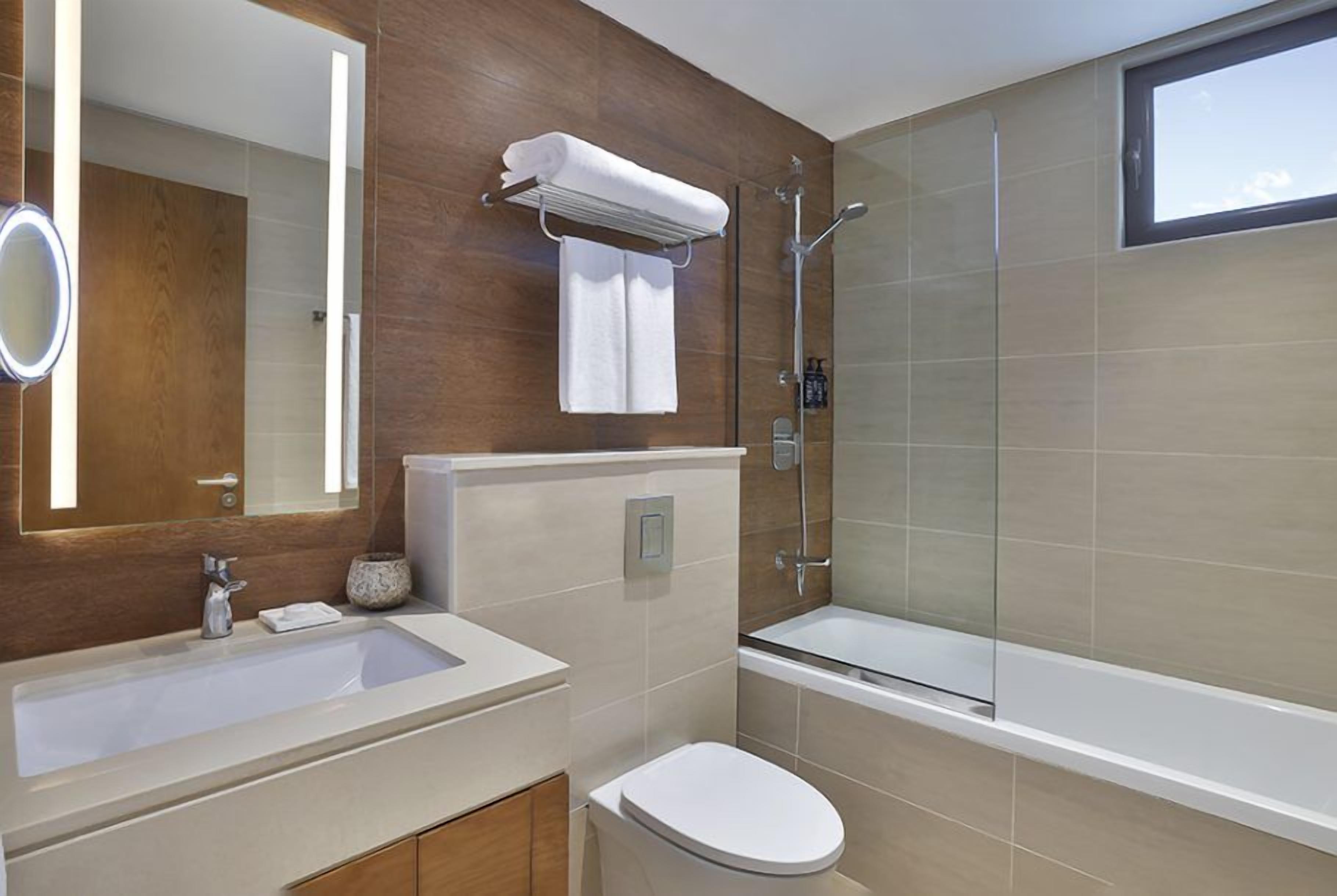 A modern bathroom with a large mirror, a sink, a toilet, and a glass-enclosed shower.