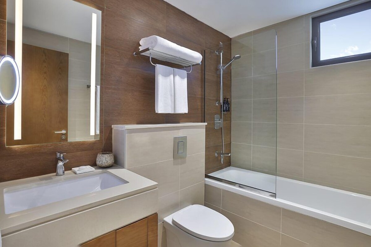 A modern bathroom with a large mirror, a sink, a toilet, and a glass-enclosed shower.