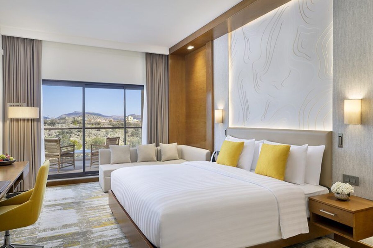 A hotel room with a large bed, a desk, a chair, and a view of the desert.