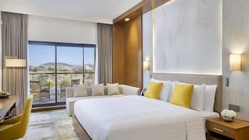 A hotel room with a large bed, a desk, a chair, and a view of the desert.