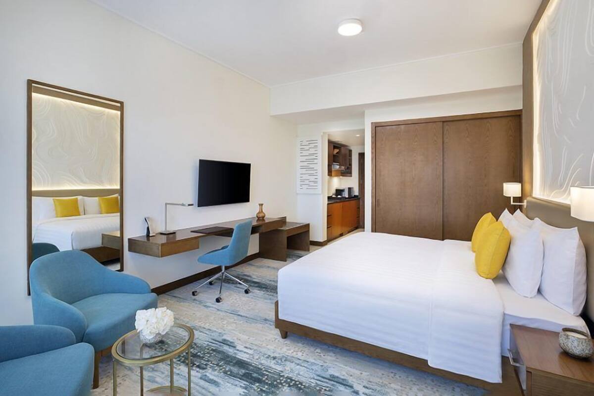 A hotel room with a large bed, a desk, a chair, a TV, and a small table.