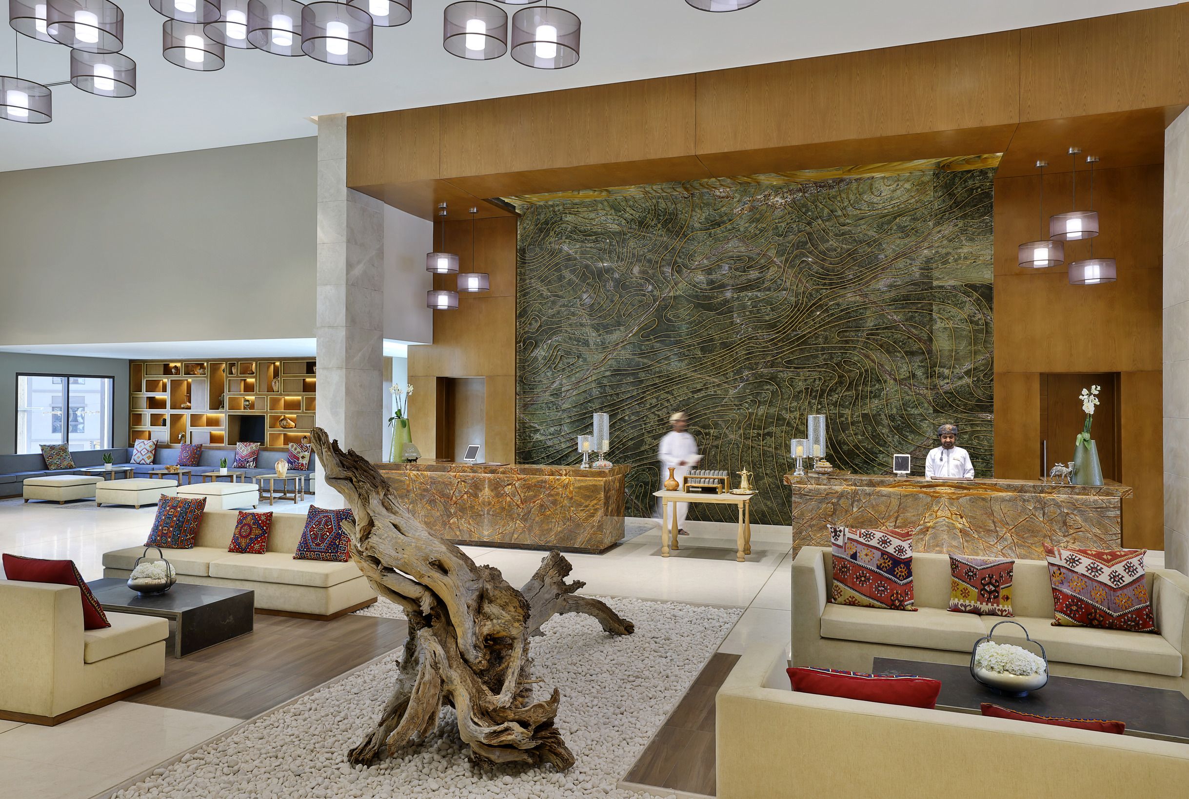 A spacious lobby with a reception desk, sofas, a large decorative wall, and a wooden tree trunk centerpiece.