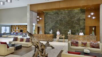 A spacious lobby with a reception desk, sofas, a large decorative wall, and a wooden tree trunk centerpiece.