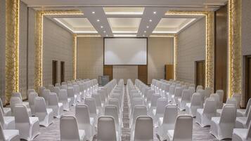 A conference room with rows of white chairs, a large screen, and a carpeted floor.
