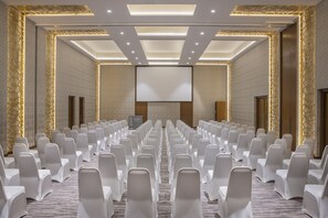 Ein Konferenzraum mit Reihen weißer Stühle, einer großen Leinwand und einem Teppichboden.