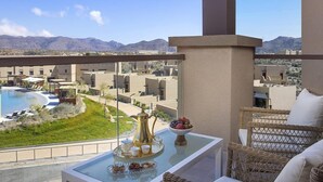 Varanda com mesa posta para chá, uma tigela de frutas e vista para uma piscina e edifícios ao longe.
