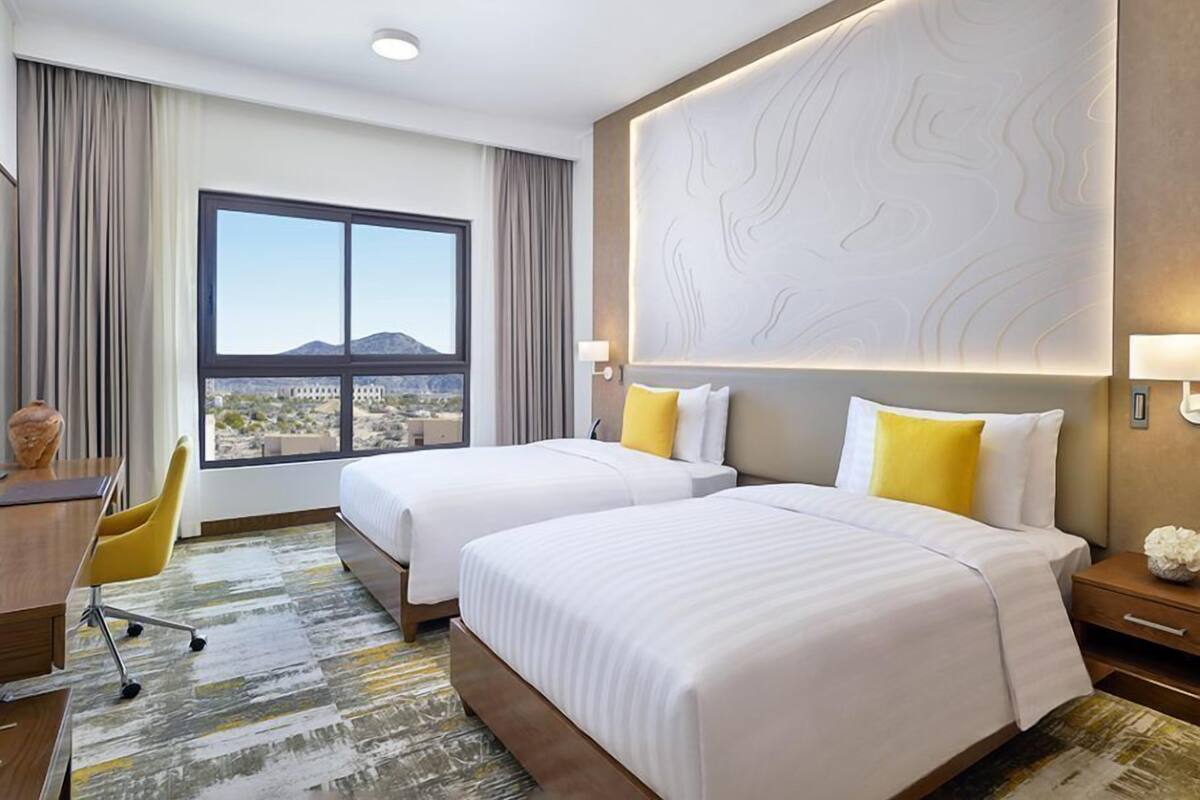 A hotel room with two beds, a desk, a chair, and a large window with a view.