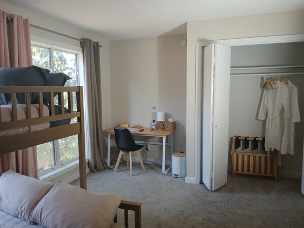 Un dormitorio con una cama litera, un escritorio con silla, un armario blanco y una mesita.