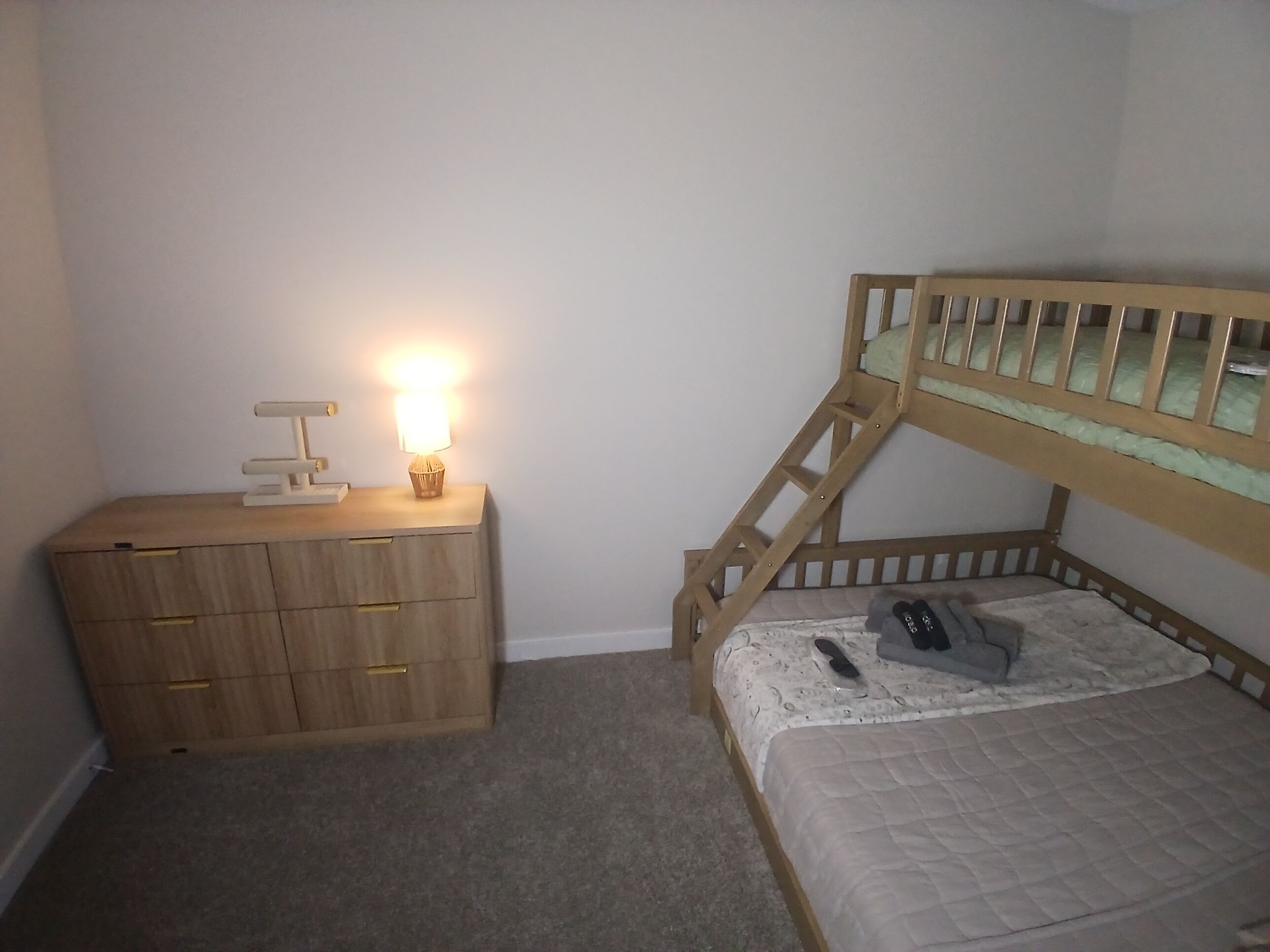 A bedroom with a bunk bed, a bedside table with a lamp, and a dresser with drawers.