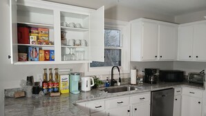 Une cuisine moderne avec des meubles blancs, un plan de travail en granit, un lave-vaisselle, une machine à café et divers appareils de cuisine.