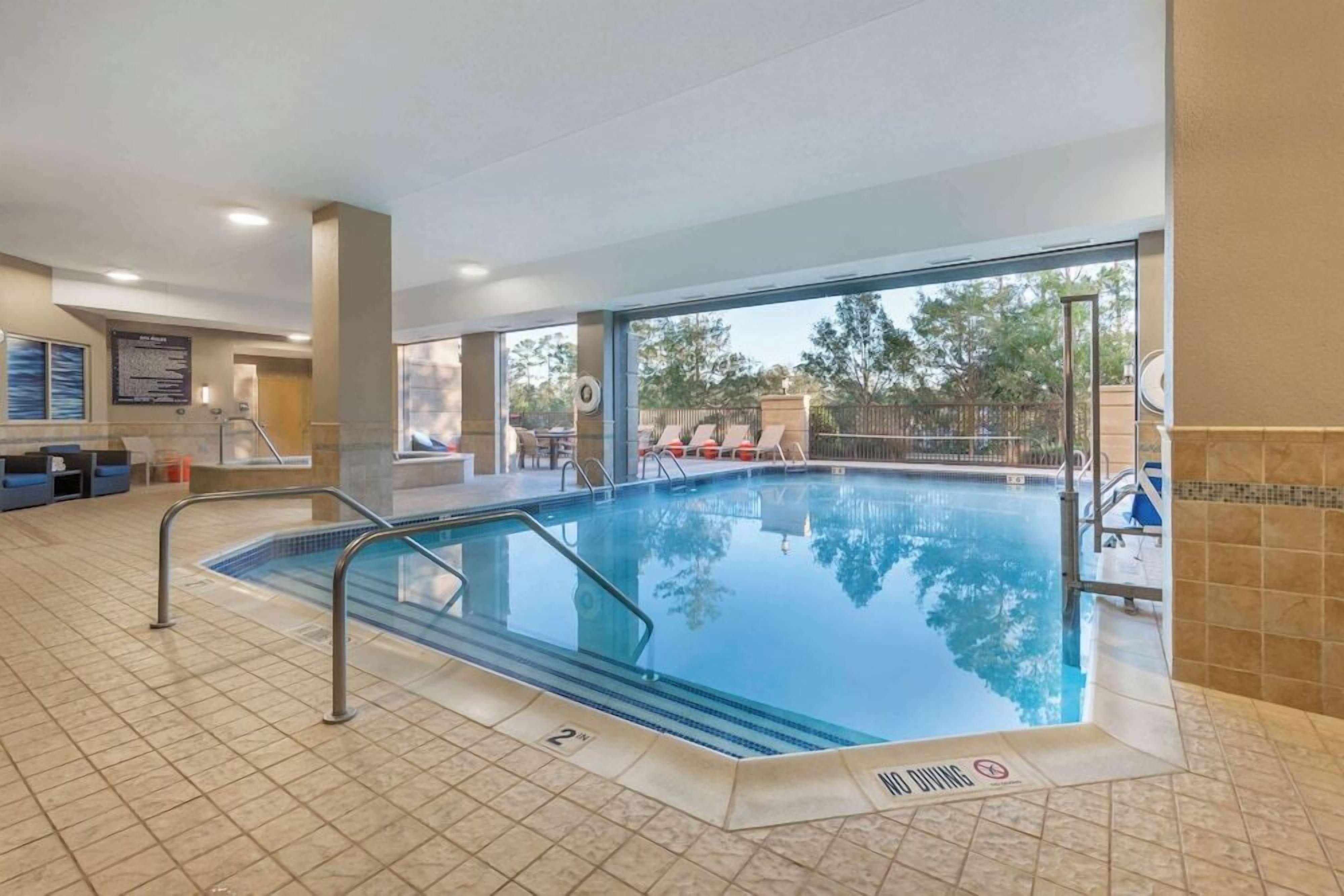 Une piscine intérieure avec des parois en verre transparent, un sol carrelé et un panneau indiquant qu’il est interdit de plonger.