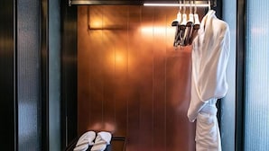 Ein Hotelzimmer mit einer Wandpaneele aus Holz, einem Bademantel, der auf einem Gestell hängt, und einer Ablage mit Hausschuhen.