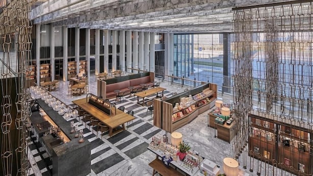 Eine großzügige Lobby mit Schachbrettmuster-Boden, Sitzbereichen, einer Bar und Blick ins Freie durch große Fenster.