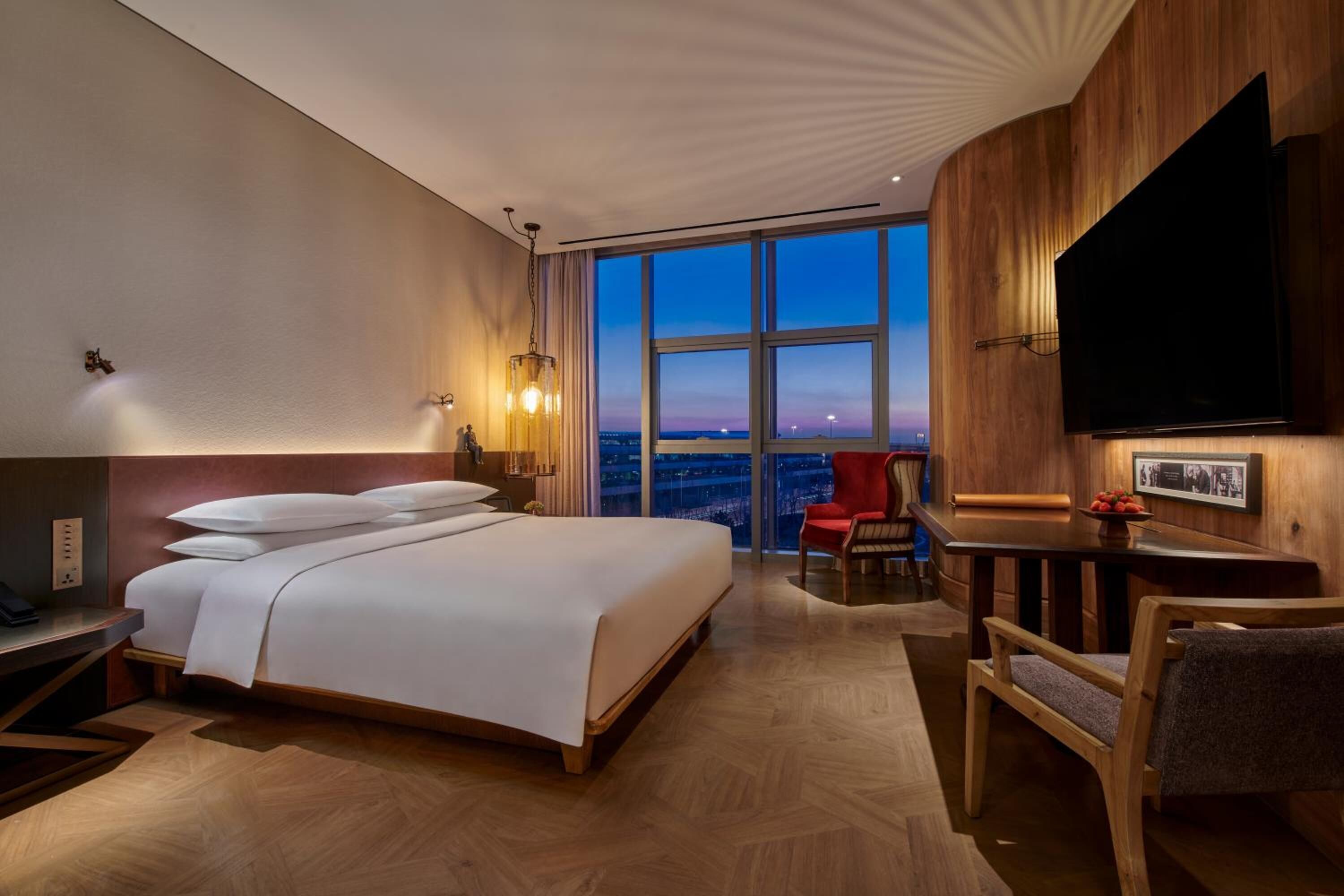 Habitación de hotel con una cama grande, un escritorio, una silla, un televisor y vistas a la ciudad.