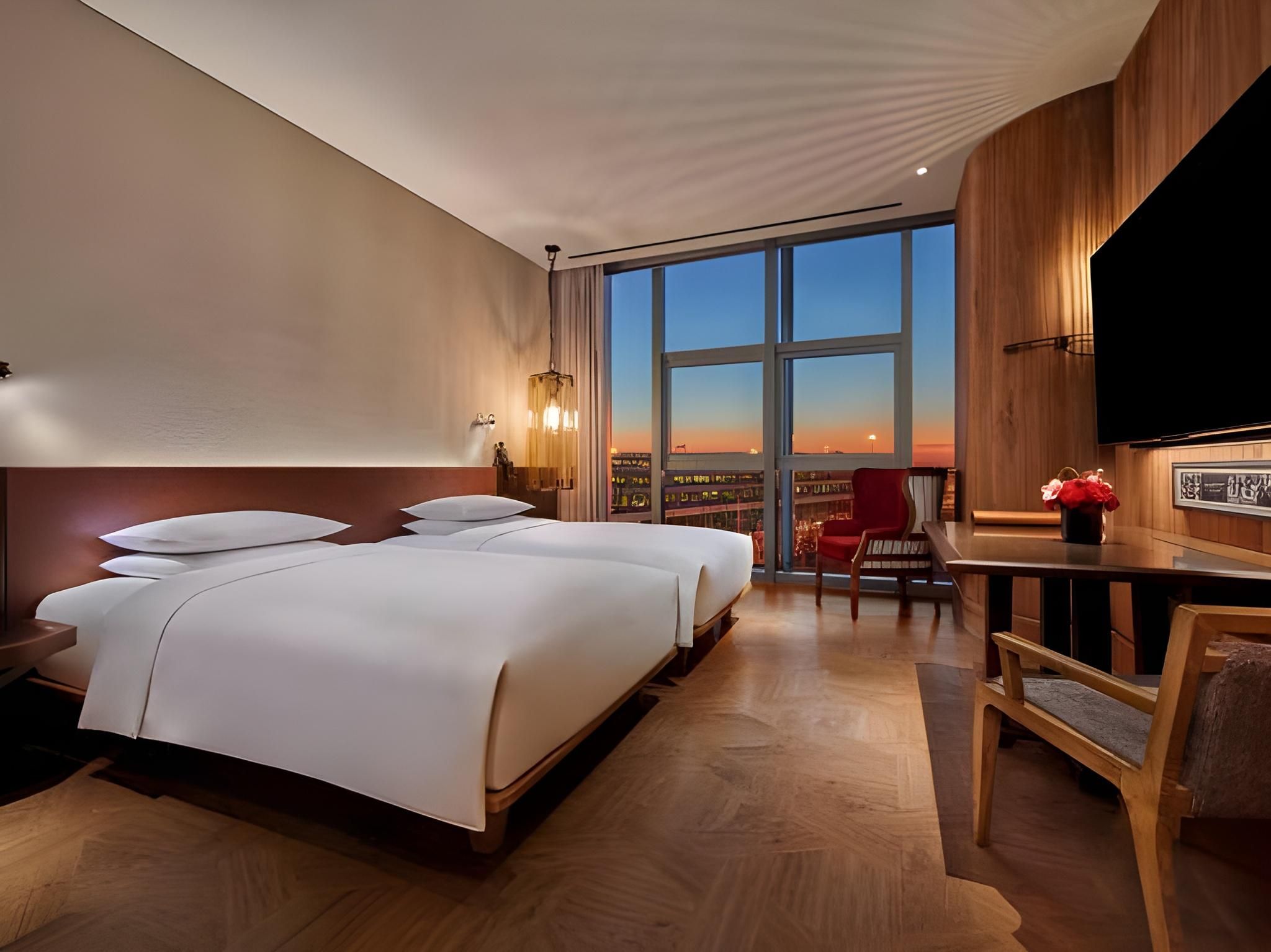A hotel room with a large bed, a desk, a chair, and a TV.