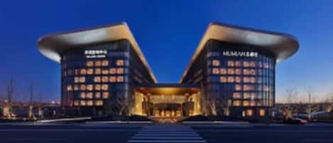 A modern hotel with a symmetrical facade, featuring two prominent towers with illuminated windows and a central entrance.