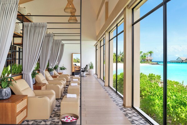 A hotel room with a view of the ocean, a seating area with chairs and a table, and a reception desk. - Hilton Maldives Amingiri Resort and Spa (Amingiri)