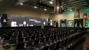 An auditorium with rows of chairs facing a stage with a large screen displaying text and graphics. - Vila Gale Alagoas (Barra de Santo Antonio)