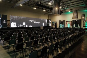 An auditorium with rows of chairs facing a stage with a large screen displaying text and graphics. - Vila Gale Alagoas (Barra de Santo Antonio)