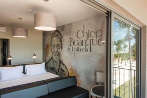 Ein Schlafzimmer mit einem großen Bett, einem Schreibtisch und einem Stuhl. An der Wand befindet sich ein Wandgemälde mit Text und einem Porträt.