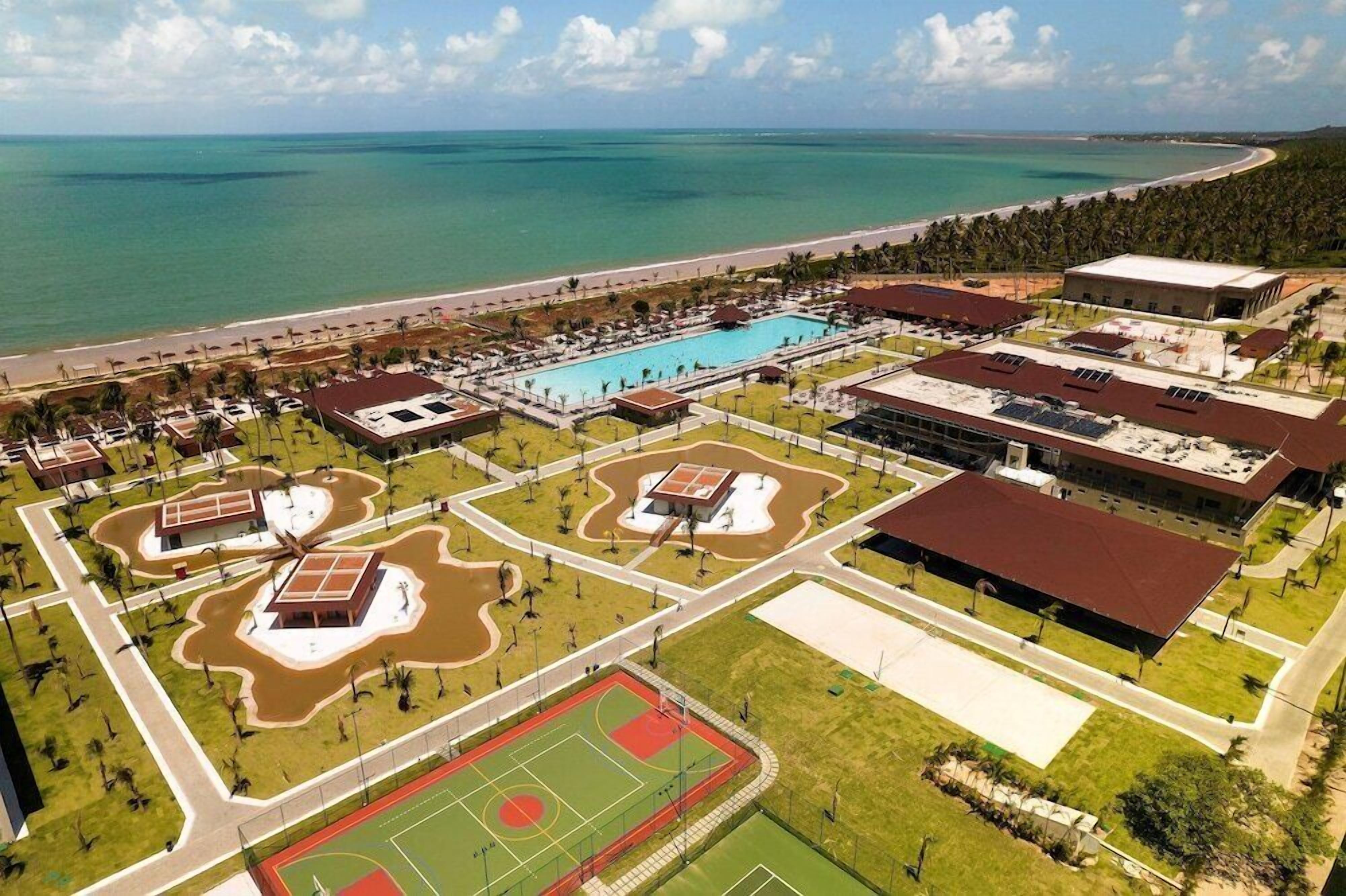 Vista aérea de um resort com piscina, quadras de tênis e uma praia.