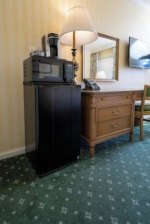 A compact hotel room with a kitchenette area featuring a microwave, coffee maker, and telephone. A wooden dresser with drawers and a chair are also visible. - Little America Hotel Wyoming (Little America)