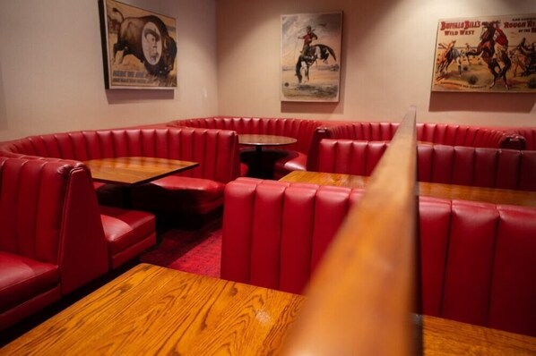 Un restaurant avec des banquettes rouges et des tables en bois, dont la décoration murale est sur le thème des cowboys.