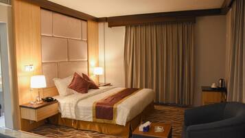 A hotel room with a bed, two bedside lamps, a nightstand, a chair, a small table, and a window with curtains.