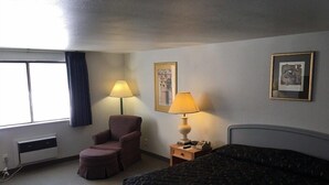 A hotel room with a bed, a chair, a desk with a lamp, and a window with curtains. - Americas Best Value Inn Billings (Billings)