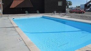 A rectangular swimming pool with a tiled edge, adjacent to a building with a dark brick facade and a brown awning. - Americas Best Value Inn Billings (Billings)