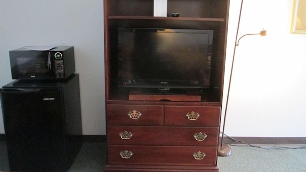 A wooden entertainment center with a flat-screen TV, a microwave, and a small refrigerator. - Americas Best Value Inn Billings (Billings)