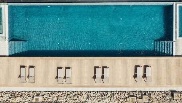 Una piscina rectangular con agua azul cristalina, rodeada por una terraza de madera con sillas de descanso.