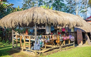 Uma cabana com telhado de palha e cerca de madeira, exibindo diversos sacos coloridos feitos de tecido e remos de madeira.