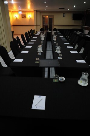 A conference room with a long table, chairs, and various items like glasses, papers, and a pitcher. - Huon Gulf Hotel and Apartments (Lae)