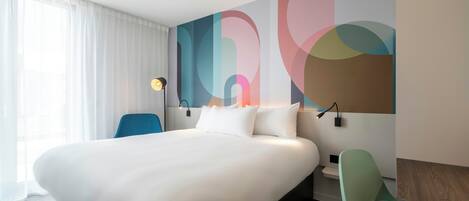 A hotel room with a large bed, a desk, a chair, and a wall with abstract art.