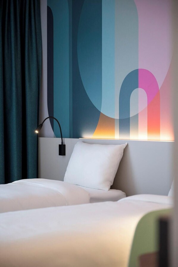 A modern hotel room with a bed, a nightstand, a wall-mounted lamp, and a large abstract wall art piece. - B&B Hotel Antwerp Centre (Antwerp)