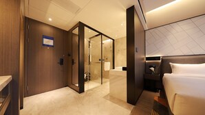 Ein modernes Hotelzimmer mit Bett, Nachttisch, einer Duschkabine aus Glas und einem Holzschrank.