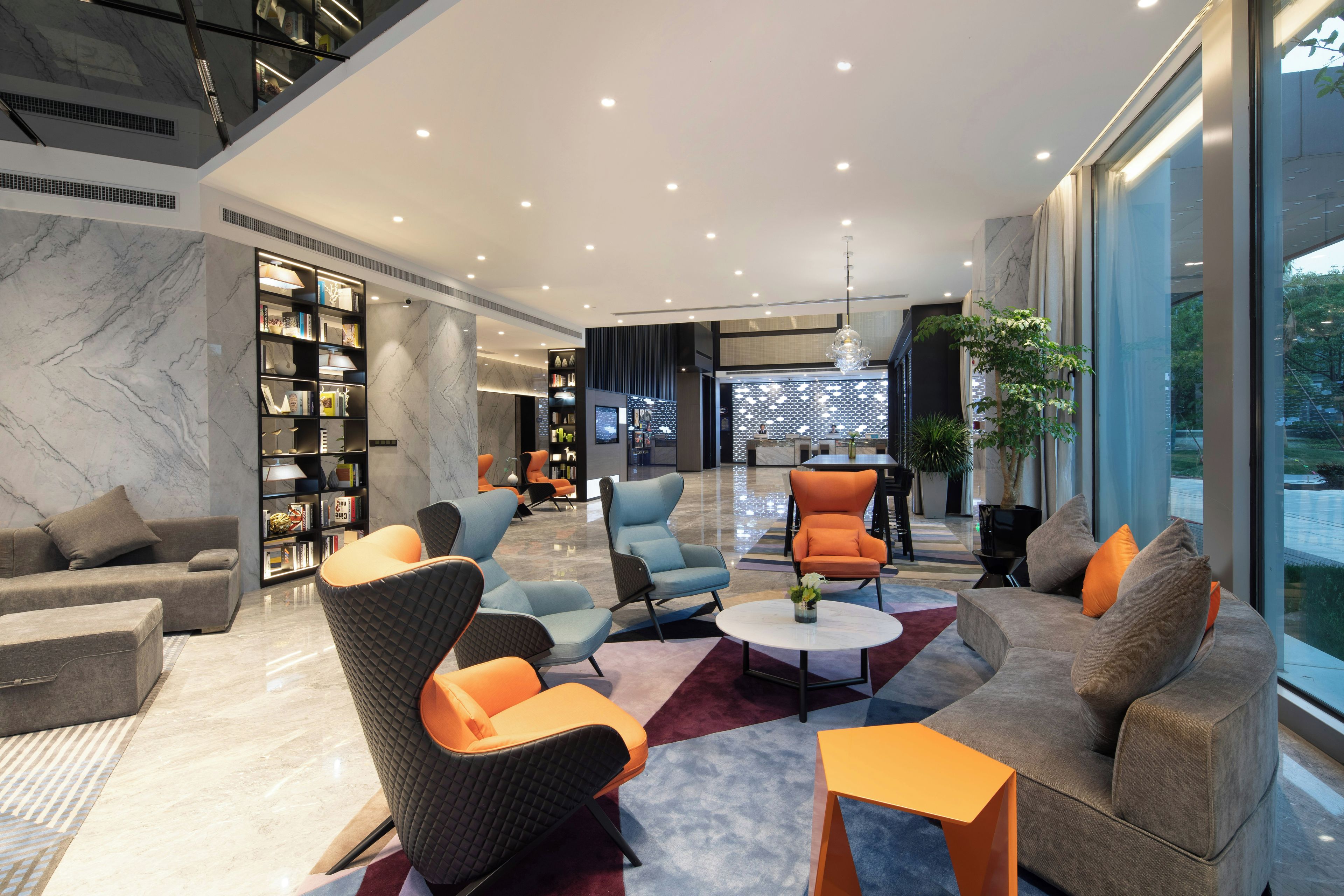 A modern lobby with seating, a large bookshelf, and a large window with a view.