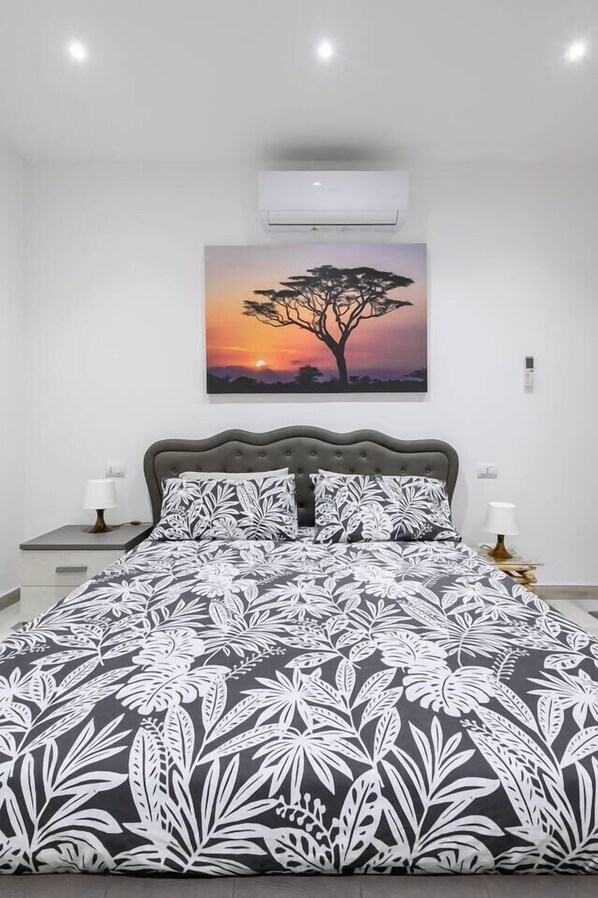 A bedroom with a bed, two bedside tables, a wall-mounted air conditioner, and a painting of a tree at sunset. - Africa Suite Marconi WiFi Fast Self Check-in (Roma)