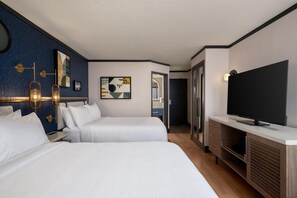Quarto de hotel com duas camas, televisão, escrivaninha e banheiro visível através de uma porta aberta.